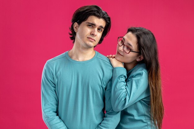 Young couple on valentines day pleased girl looking at sad guy isolated on pink background