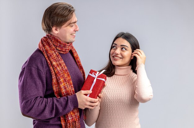 Young couple on valentines day pleased guy giving gift box to smiling girl looking at each other isolated on white background