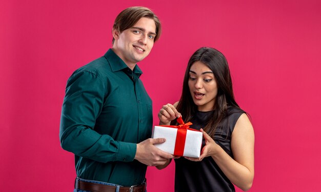 발렌타인 데이에 젊은 부부는 분홍색 배경에 고립 된 놀란 소녀에게 선물 상자를주는 웃는 남자