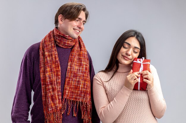 Молодая пара на день святого валентина улыбающийся парень смотрит на довольную девушку с подарочной коробкой на белом фоне