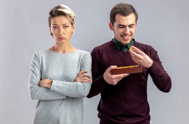 Young couple on valentines day unpleased girl standing next to guy with box of candies isolated on white background