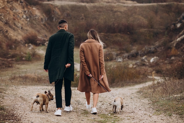 Free photo young couple walking their french bulldogs in park