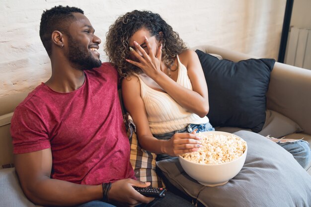 Young couple watching a horror movie while sitting on a couch at home.