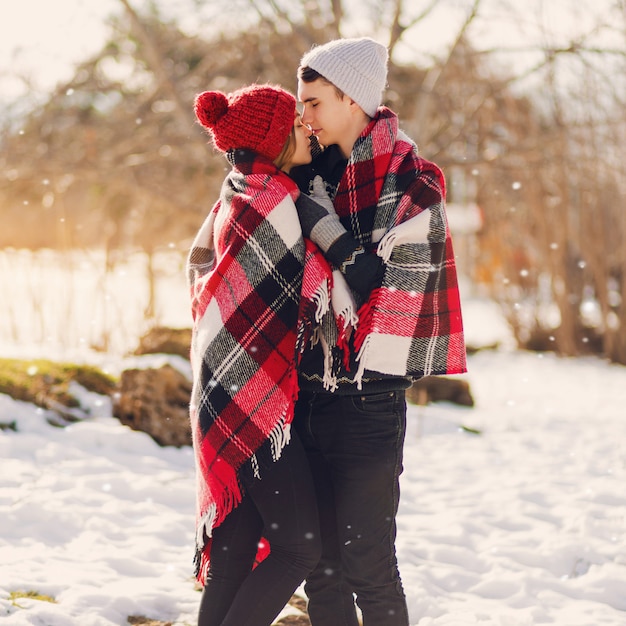 Young couple wearing blanket ad kissing on a snowy field