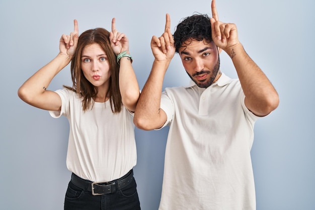 Foto gratuita giovane coppia che indossa abiti casual in piedi insieme facendo un gesto divertente con il dito sopra la testa come corna di toro