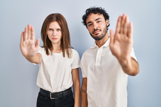 Free photo young couple wearing casual clothes standing together doing stop sing with palm of the hand. warning expression with negative and serious gesture on the face.