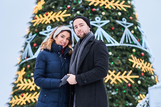 Young couple wearing standing near a city Christmas tree, enjoying spending time together