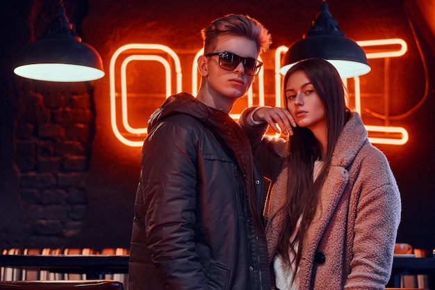 Молодая пара в стильной одежде стоит вместе в кафе с индустриальным интерьером