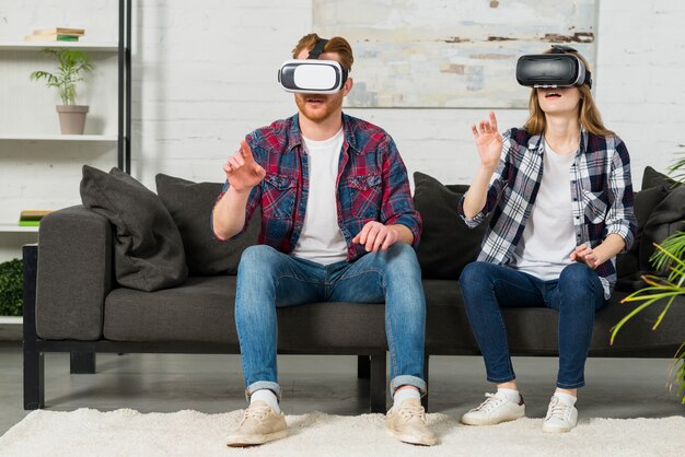 Young couple wearing virtual reality goggles touching in the air with hands