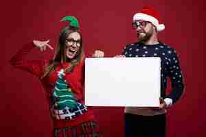 Free photo young couple in weird christmas clothes holding blank paper