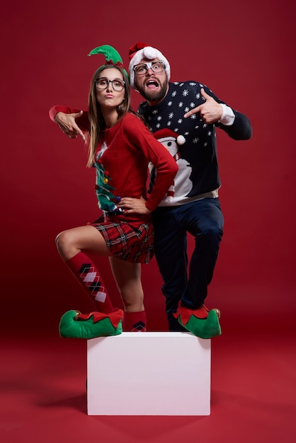 Young couple in weird Christmas clothes stepping on blank cube