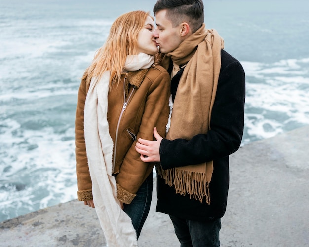 Free photo young couple in winter kissing by the beach