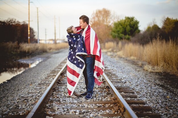 Young couple with the American flag around their shoulders standing on the railway