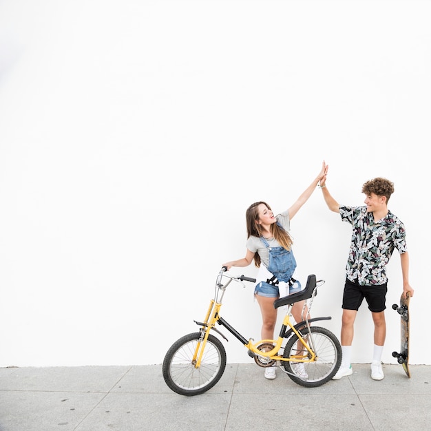 Young couple with bicycle and skateboard giving high five