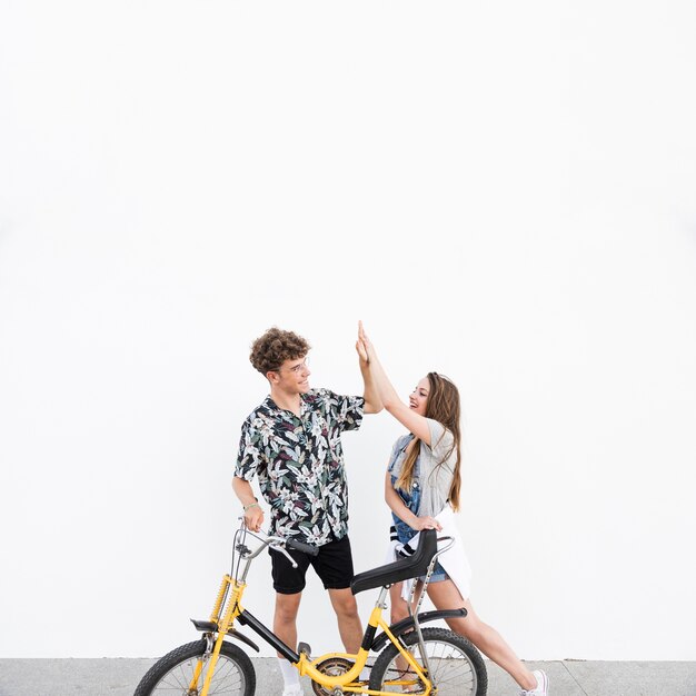 Young couple with bicycle standing on sidewalk giving high five