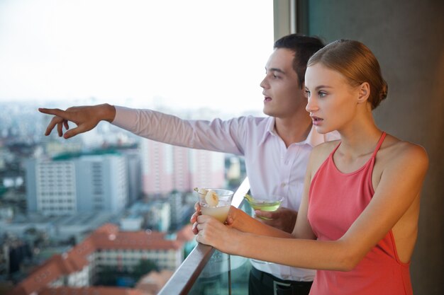 Молодая пара с коктейлем, стоя на балконе