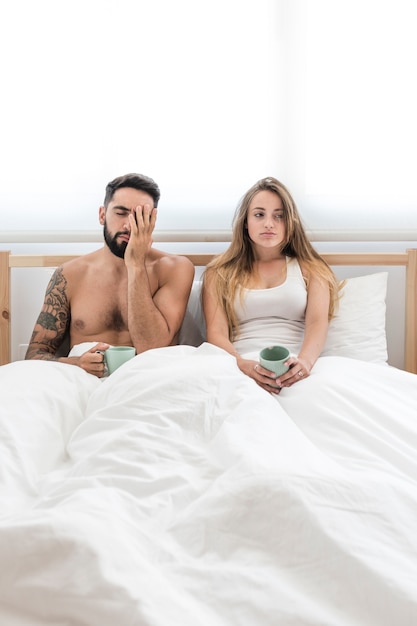 Young couple with cup of coffee sitting on bed