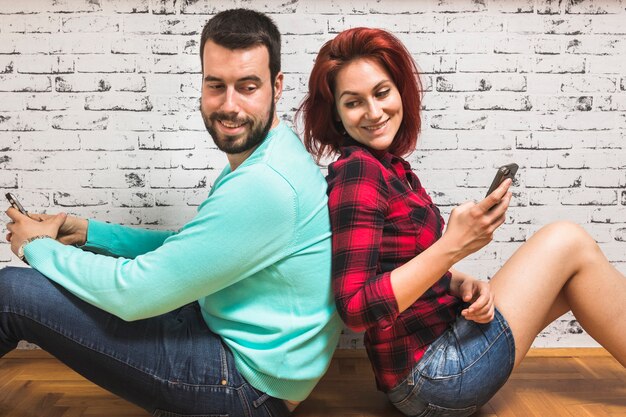 Молодая пара с мобильным телефоном, сидящим спиной к спине