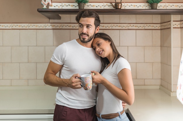 Free photo young couple with mugs hugging in kitchen