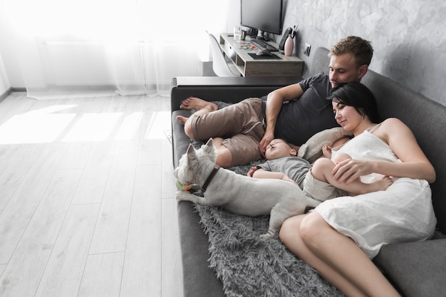 Young couple with their son and white dog lying on grey sofa at home