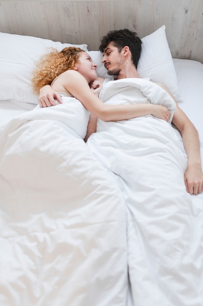 Молодая пара, завернутые в одеяло, лежа на кровати