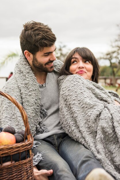Young couple wrapped in gray blanket looking at each other