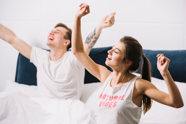 Молодая пара зевает и протягивает руки в постели