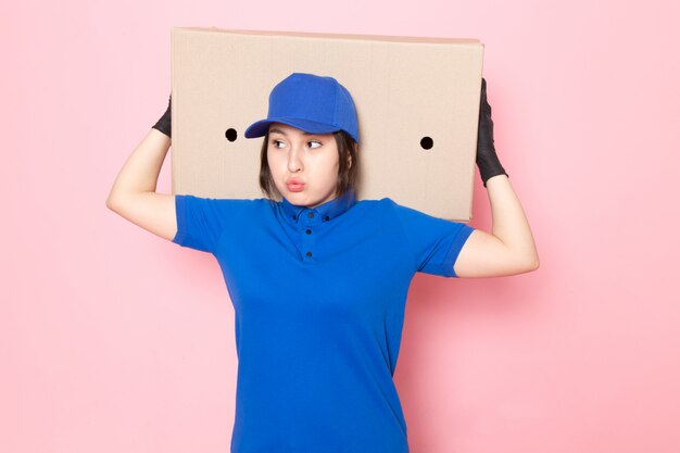 young courier in blue polo blue cap jeans holding package on pink