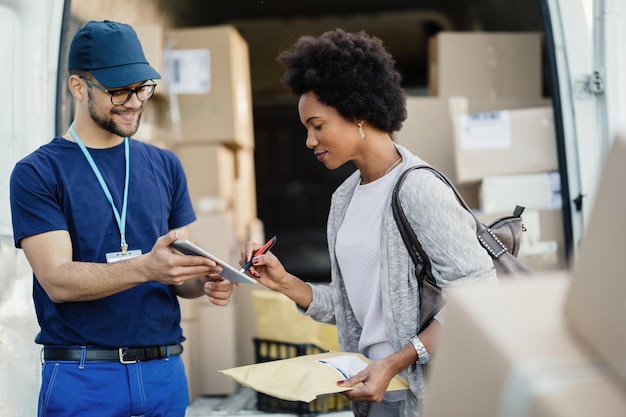 Young courier giving touchpad to a female customer to sign for a delivery Focus is on African American woman