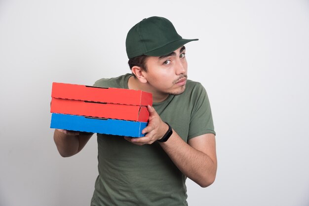 Young courier holding three boxes of pizza on white background.