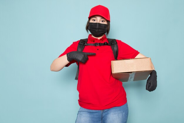 young courier in red polo red cap black sterile protective mask black backpack holding package on blue