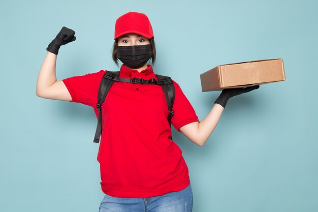 Free photo young courier in red polo red cap black sterile protective mask black backpack holding package on blue