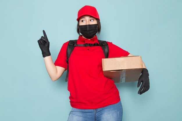 young courier in red polo red cap black sterile protective mask black backpack holding package on blue