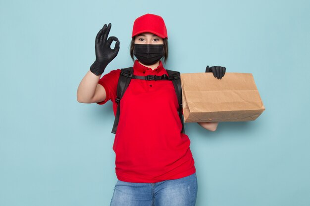 young courier in red polo red cap black sterile protective mask black backpack holding package on blue