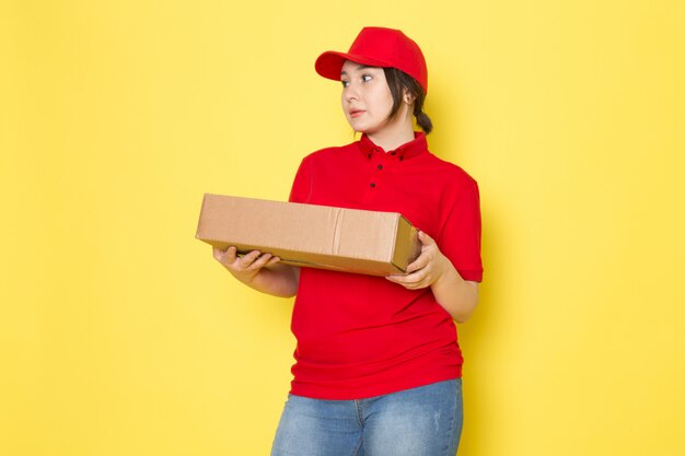 young courier in red polo red cap blue jeans holding package on yellow