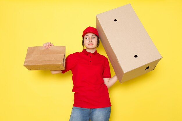 young courier in red polo red cap holding package and box smiling on yellow