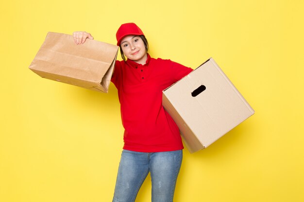 young courier in red polo red cap holding package and box smiling on yellow