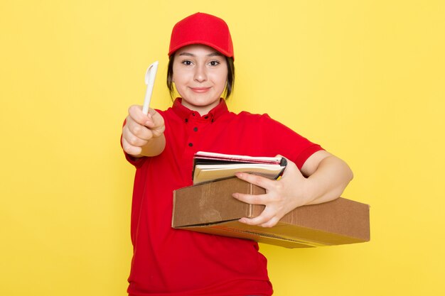 young courier in red polo red cap holding package pen copybook smiling on yellow