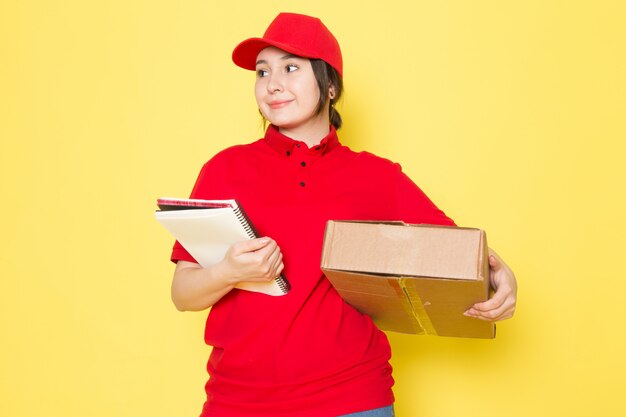 young courier in red polo red cap holding package smiling on yellow