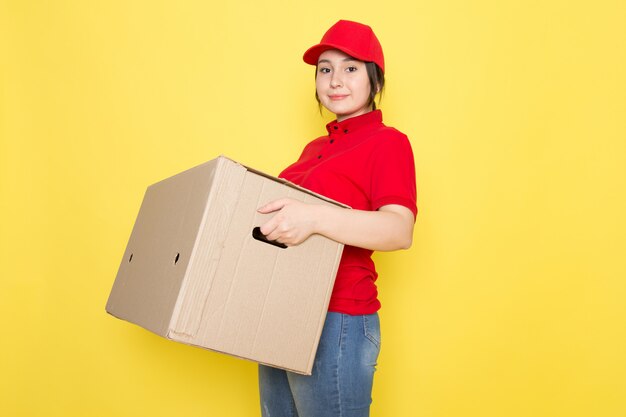 young courier in red polo red cap holding package smiling on yellow