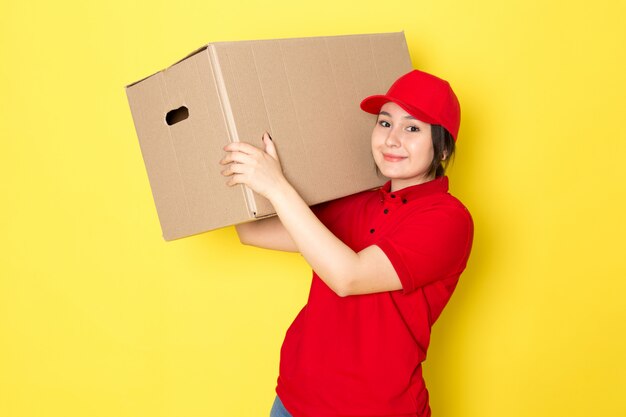 黄色に笑みを浮かべてパッケージを保持している赤いポロ赤い帽子の若い宅配便