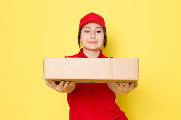 young courier in red polo red cap holding package smiling on yellow