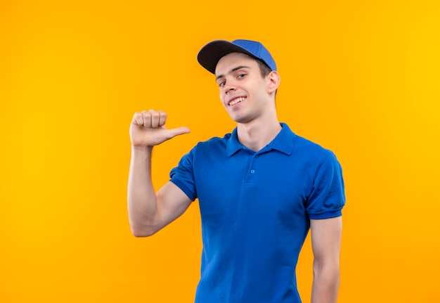 Free photo young courier wearing blue uniform and blue cap doing happy thumbs on himself