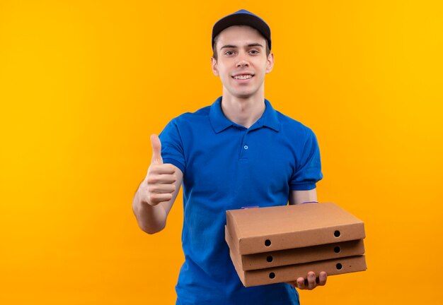 Young courier wearing blue uniform and blue cap doing happy thumbs up