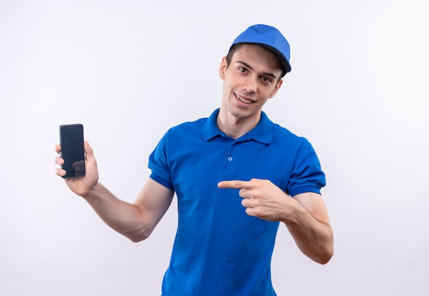 Il giovane corriere che indossa l'uniforme blu e il cappuccio blu indica felicemente sul telefono