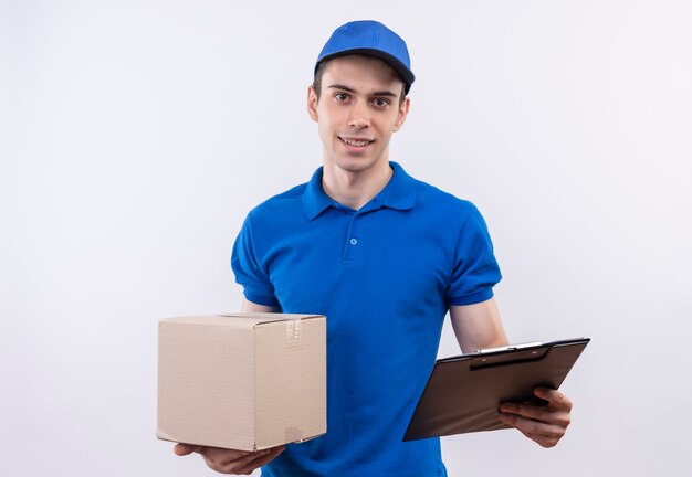 箱とクリップボードを保持している青い制服と青い帽子を身に着けている若い宅配便