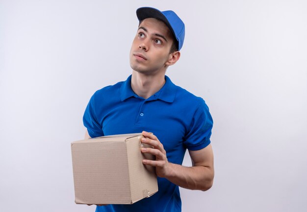 Young courier wearing blue uniform and blue cap holds a box