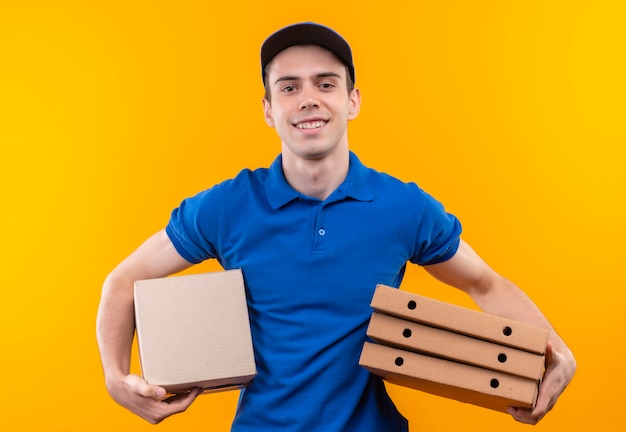 Young courier wearing blue uniform and blue cap holds boxes