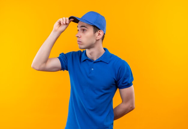 Young courier wearing blue uniform and blue cap looks besides confused