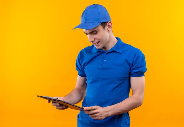 Young courier wearing blue uniform and blue cap looks at the clipboard